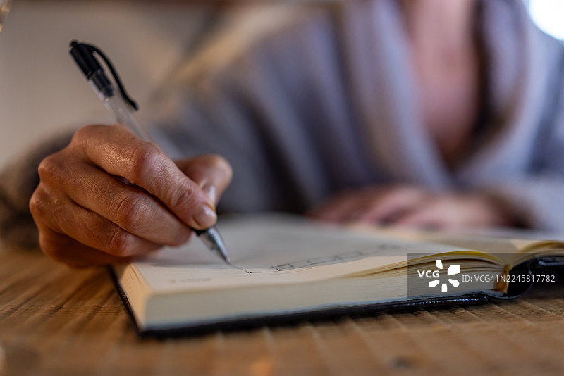 特写：桌面上，手持钢笔在笔记本上书写图片素材