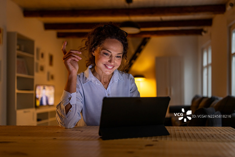 居家女性微笑使用平板，舒适的客厅环境，暖色调灯光图片素材