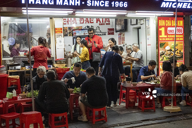 越南河内，人们坐在餐厅外的路边低矮塑料凳上，享用街头美食，社交互动。图片素材
