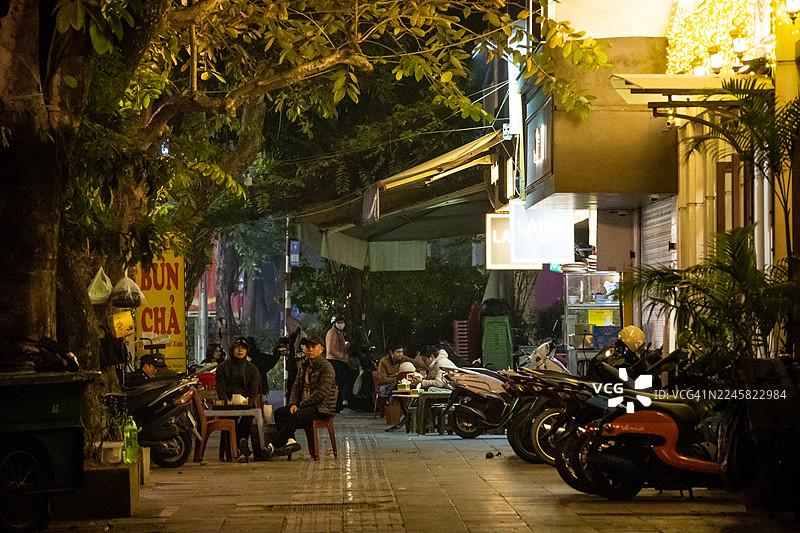 越南河内，餐厅门前的路边座位上，食客们在熙熙攘攘的街头氛围中享受户外用餐。图片素材