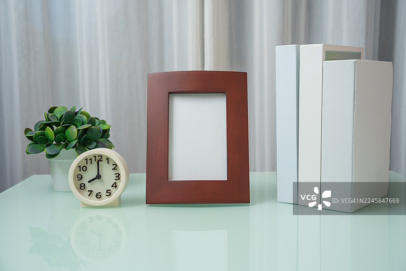 摆放在桌上的家居装饰。客厅的室内设计，木架上摆放着闹钟、精美的盆栽植物、相框和书籍，装饰简约。图片素材