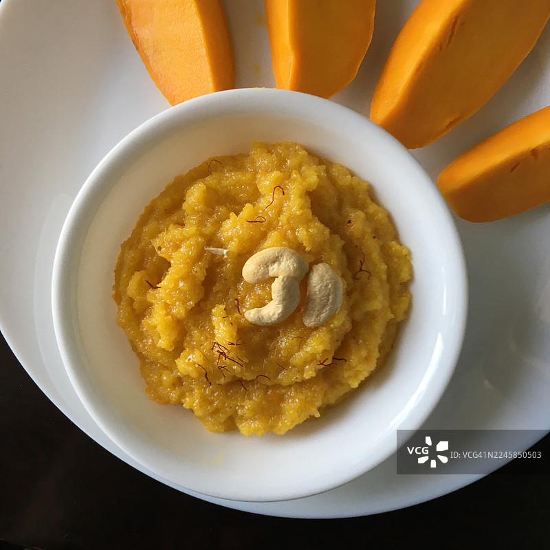 白色盘子里的芒果哈尔瓦甜点，配有芒果片。图片素材