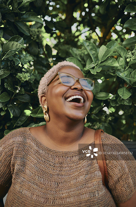 戴着眼镜和夸张耳环的年轻创意黑人女性在户外大笑图片素材