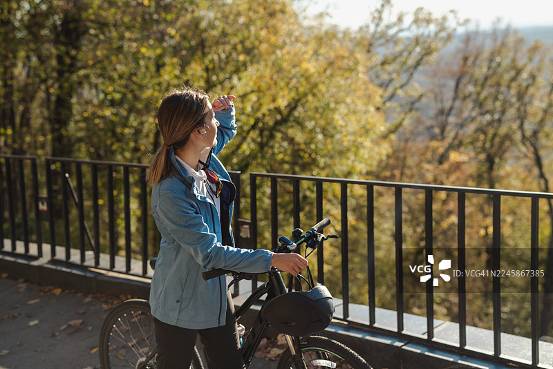 秋日公园里，一位女士在阳光明媚的午后骑着自行车享受骑行图片素材