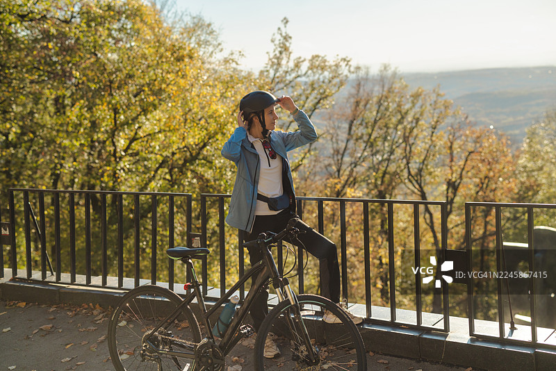 一位戴着头盔、穿着休闲夹克的女士在秋季的观景点骑自行车图片素材