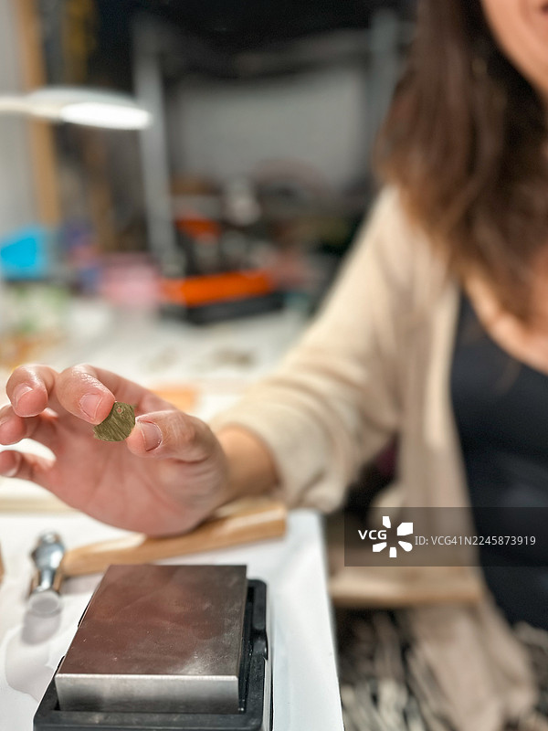 特写：珠宝工匠手持金色鸟形金属件制作耳环图片素材