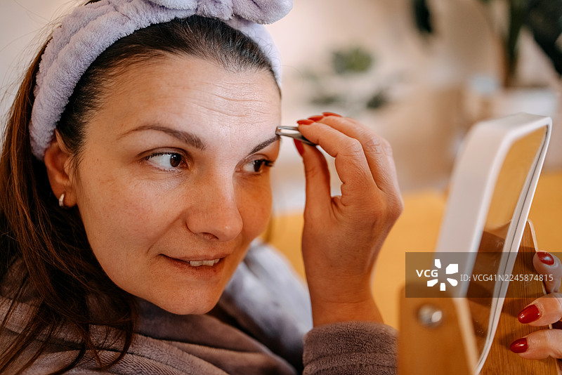 女人坐在客厅沙发上，修饰眉毛并护理肌肤。图片素材