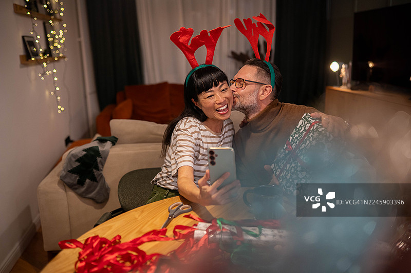 一对情侣用手机自拍或进行视频通话，背景有圣诞礼物图片素材