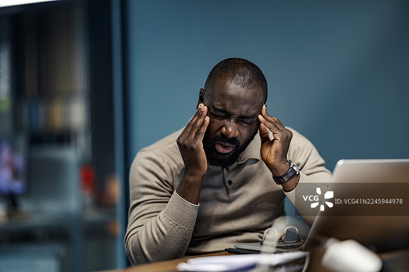 一名男子在办公室经历严重的头痛和工作压力图片素材