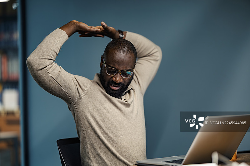 疲惫的黑人男子在办公桌前伸展身体图片素材