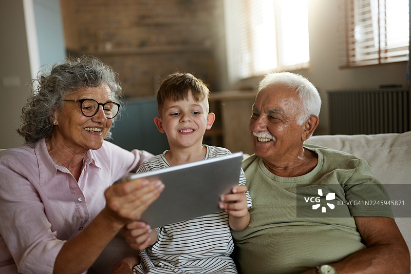 快乐的祖父母和他们的孙子在家使用触摸板。图片素材