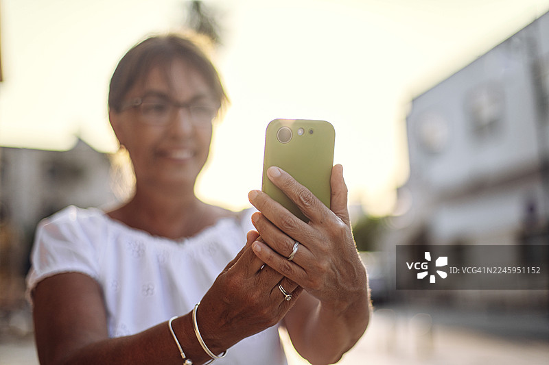 一位快乐的中年女性在黄金时刻于户外使用手机的肖像图片素材
