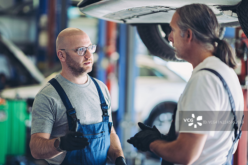 两位机械师在车库里在一辆被举起的汽车旁交谈图片素材