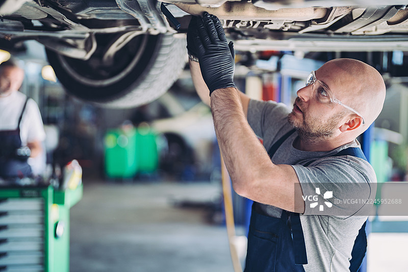 汽车维修技师正在维修举升在平台上的汽车图片素材