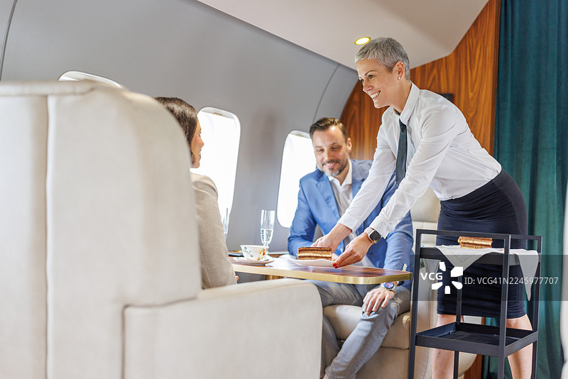 私人飞机上，空乘人员为商务人士提供甜点图片素材