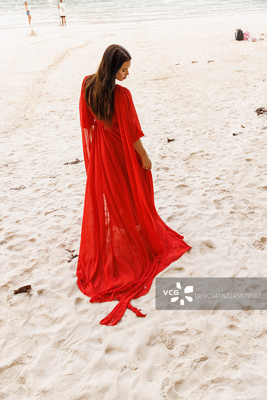 身穿红裙的女子走在沙滩上，背景是宁静的海洋图片素材