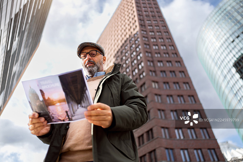 中年男性游客在柏林波茨坦广场阅读旅游指南，背景是现代建筑图片素材