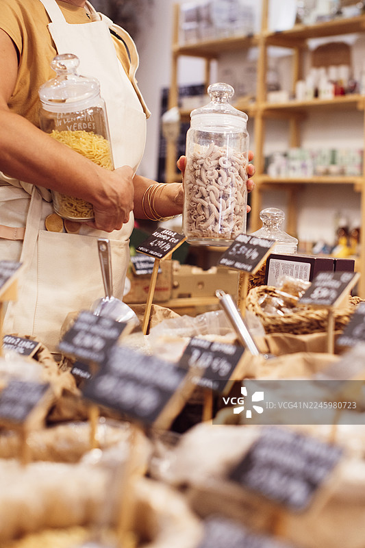 零浪费环保商店，一位穿着围裙的女士正在整理玻璃罐装食物图片素材