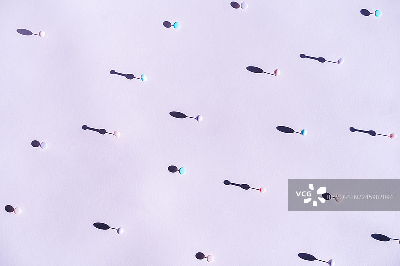 极简风格的粉彩色图钉，在直射阳光下投射出长长的阴影，在灰粉色表面上营造出空间感、孤立感和简约感。图片素材