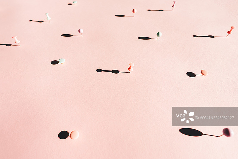 粉彩图钉的极简主义构图，在阳光直射的灰粉色表面上投下长长的阴影，营造出空间感、孤立感和简约感。图片素材