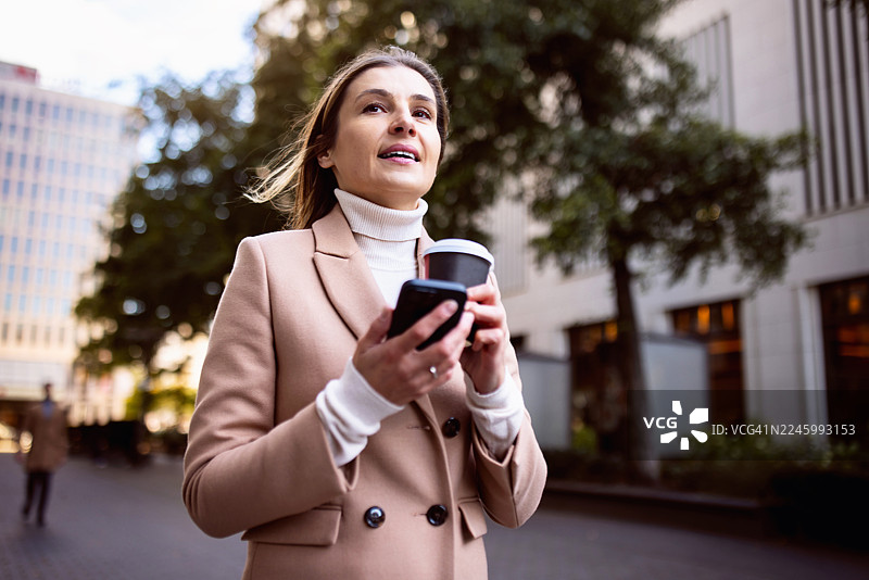 一位自信的年轻女商人，在柏林一边拿着咖啡一边使用智能手机图片素材