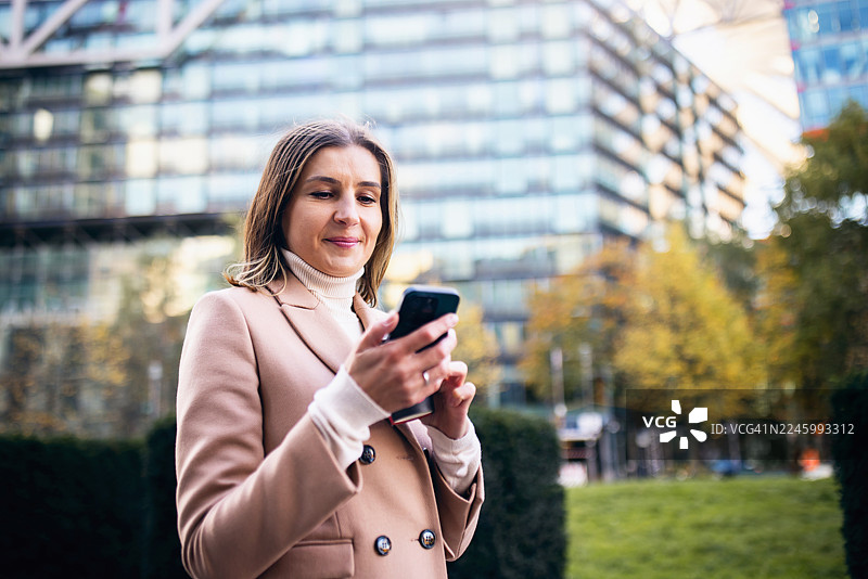 秋季，一位年轻的职业女性在柏林边走边查看智能手机图片素材