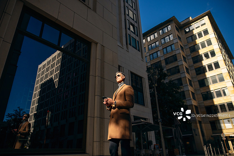 戴着太阳镜、拿着智能手机的成熟男性商务人士，沐浴在柔和的户外阴影中图片素材