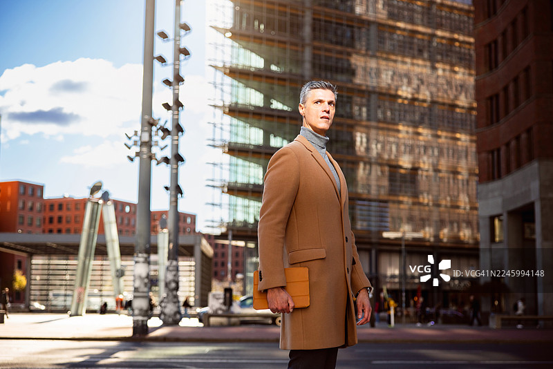 一位成熟的商人在柏林波茨坦广场的现代都市环境中，手持平板电脑行走图片素材