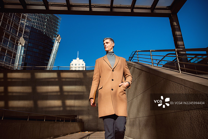 自信的商人在柏林户外，手插在时尚外套的口袋里行走图片素材