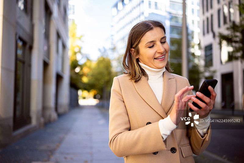 柏林城市背景下，一位女士在户外使用智能手机，面带微笑图片素材