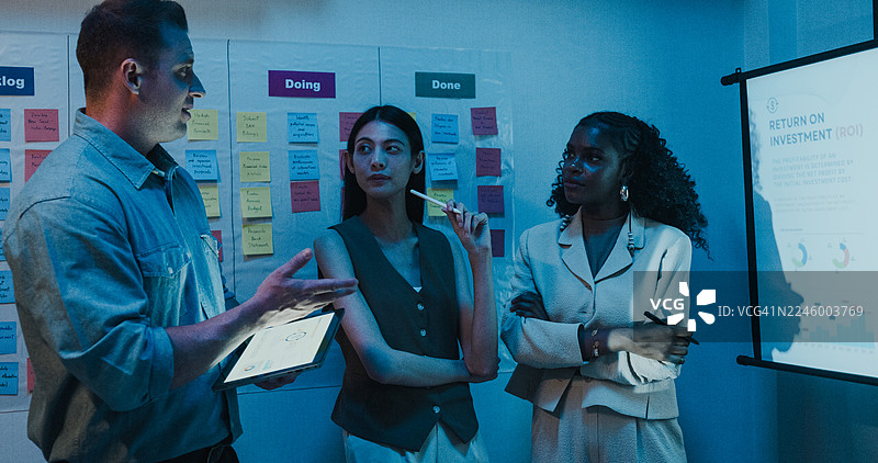 多元化的金融团队在现代办公室进行商务会议，领导者正在展示投资策略和预算规划，时间为夜晚。涉及营销策略分析、股市交易、财务顾问等概念。图片素材