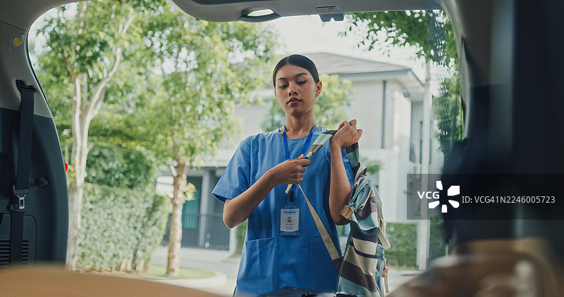 年轻的亚裔女护士穿着蓝色工作服，将包放入汽车后备箱，准备去上班。护士可持续生活方式概念。图片素材