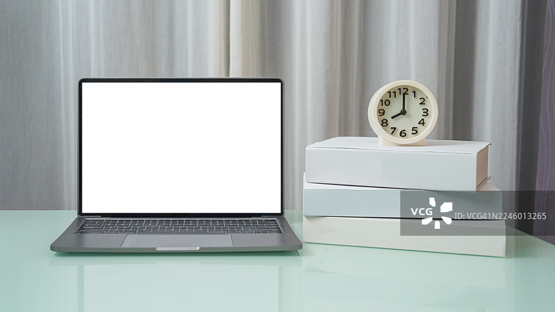 简约办公室房间，木制工作桌上放着笔记本电脑、书籍和闹钟，笔记本电脑是白色空白屏幕，房间有装饰品。图片素材
