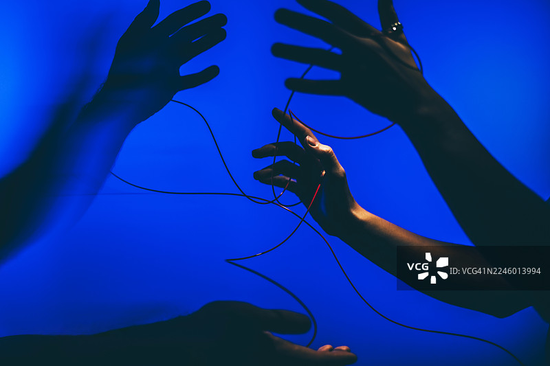 在鲜艳的纯蓝色背景下，多个人类手的深色剪影与细细的红色电线互动。这张富有戏剧性的概念图像捕捉了沟通、技术连接和数字网络的主题。图片素材