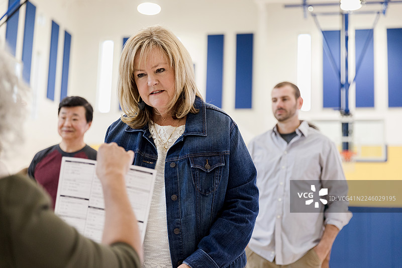 在体育馆里互动的不同种族背景的成年人，可能是在社区活动或投票站。图片素材