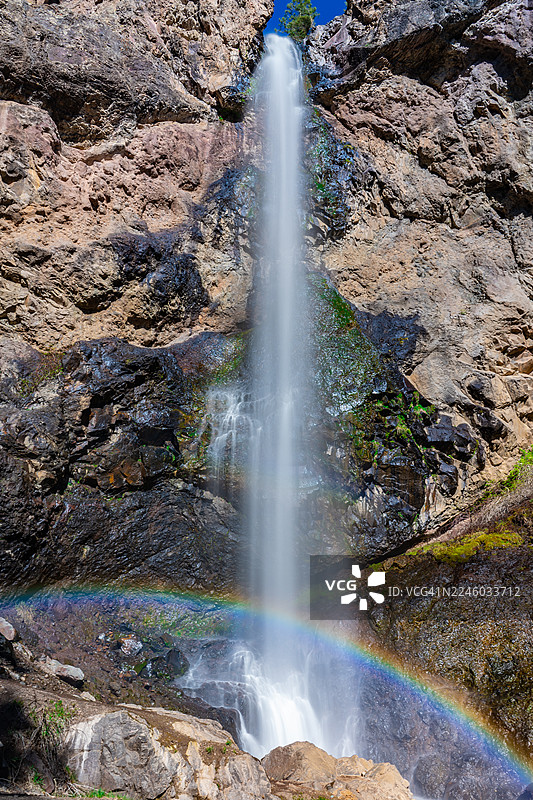 壮观的瀑布从岩石峭壁倾泻而下，一道鲜艳的彩虹横跨在水雾中，构成了一幅令人惊叹的自然奇观。图片素材