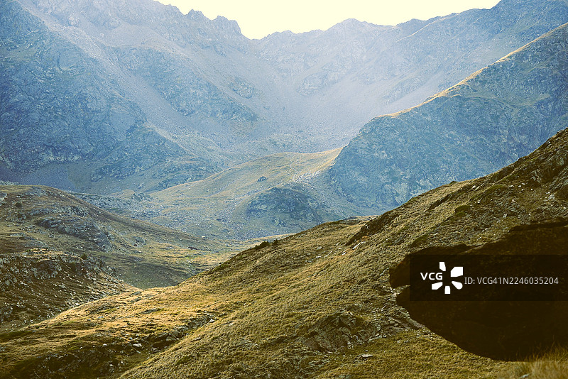 安道尔，高角度俯瞰广阔的山谷，可见岩石斜坡和零星的绿草，天空明亮图片素材