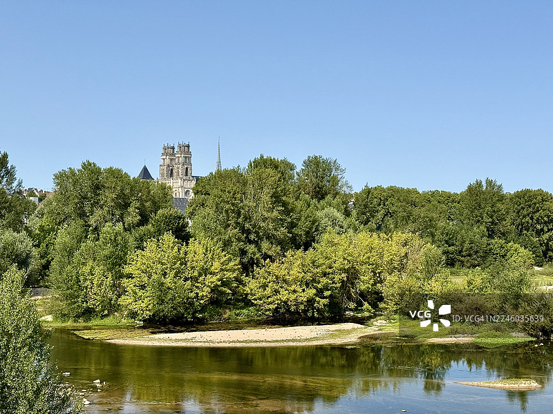 法国，乔治五世桥，一座历史悠久的教堂坐落在青翠的树木旁，旁边是一条宁静的河流，天空湛蓝，景色优美。图片素材