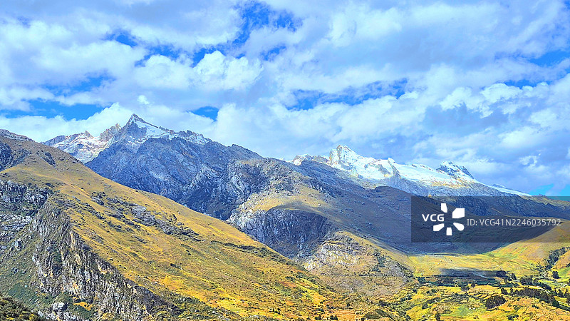 雄伟的雪山在阳光普照的山谷之上，在有蓬松白云的湛蓝天空下拔地而起，展示了高海拔景观的美丽图片素材