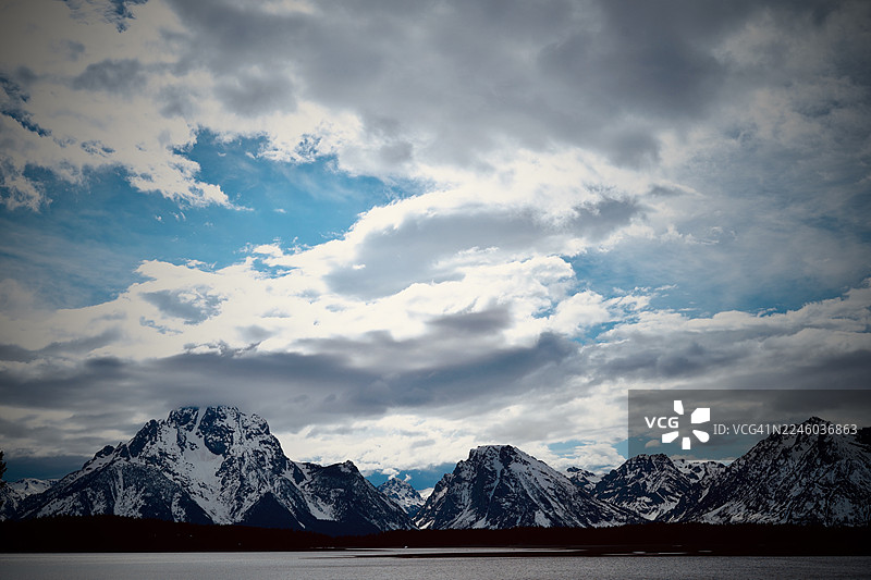 美国杰克逊，冬季戏剧性景观，白雪皑皑的山脉和多云的天空笼罩着平静的湖面图片素材