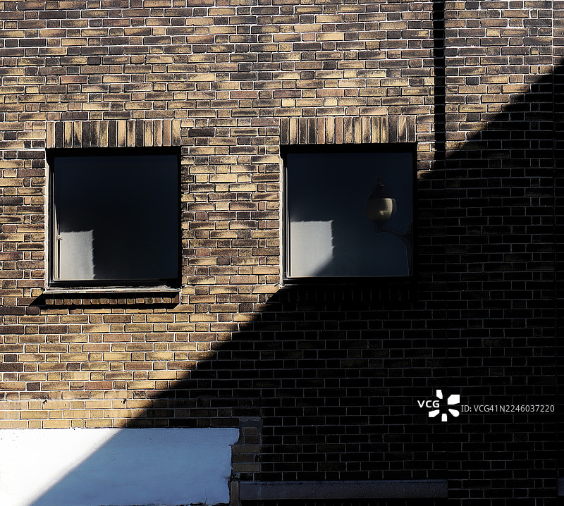 从低角度拍摄的砖墙，带有窗户、戏剧性的阴影和路灯倒影，地点：加拿大汉密尔顿图片素材
