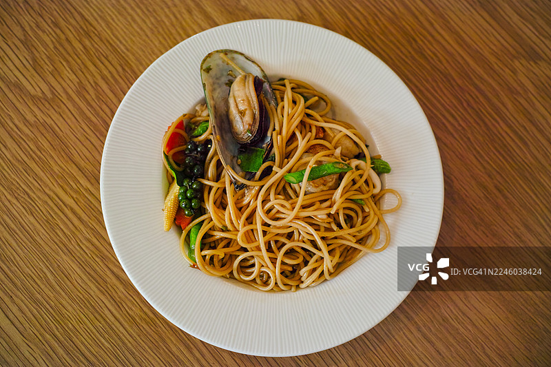 俯视角度拍摄的美味海鲜意面，上面放着一只贻贝，盛放在木桌上的白盘子里图片素材