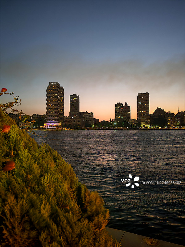 黄昏时分，城市建筑映衬着生机勃勃的夕阳天空，构成一幅河流美景。图片素材