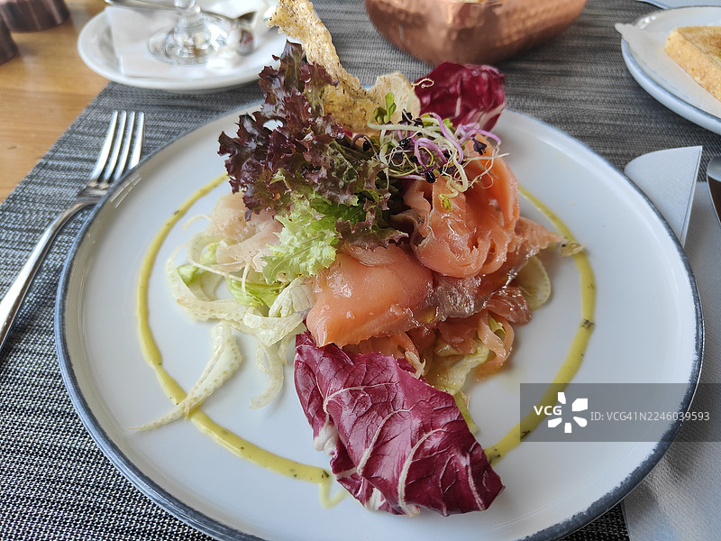 俯视角度拍摄的精致三文鱼沙拉，盛放在白盘中，摆放在餐厅餐桌上，待人享用图片素材