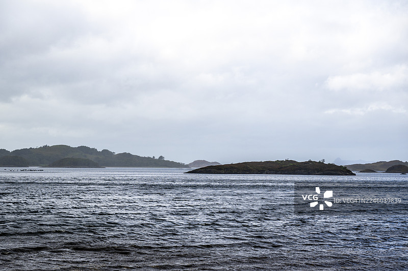 宁静的自然风光，岛屿坐落在平静的海面上，天空布满云彩，景色平和而开阔，位于英国罗斯郡和克罗默蒂地区。图片素材