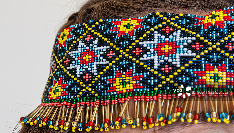 特写镜头，展示一款色彩鲜艳、图案精美、带有金色流苏的珠绣发带，由真人佩戴图片素材