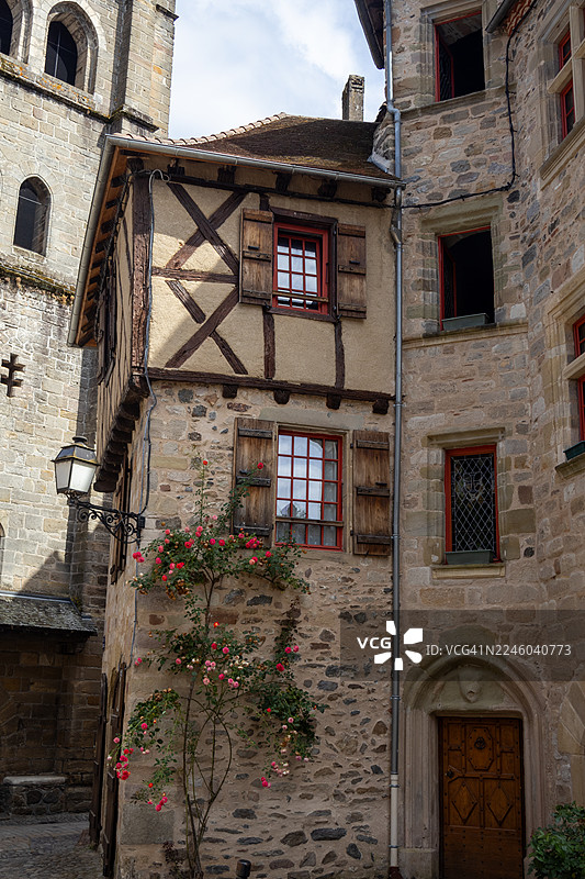 俯视角度拍摄，迷人的欧洲乡村老建筑，带有木框架和石头结构，攀附着玫瑰花，天空晴朗，地点为法国康塔尔地区。图片素材