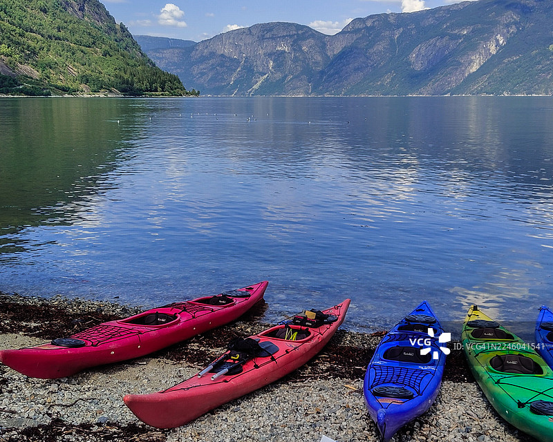 五彩的皮划艇停靠在宁静湖泊的岩石岸边，背景是雄伟的山峦和湛蓝的天空图片素材