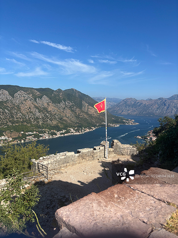 从古老要塞俯瞰科托尔湾的全景，包括远处的山脉、城镇和旗帜，天空湛蓝图片素材