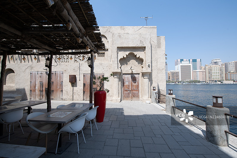 迪拜传统建筑风格的露天咖啡馆空座位区,可俯瞰现代化的迪拜城市天际线和河流,位于阿联酋迪拜的Bur Dubai区。图片素材